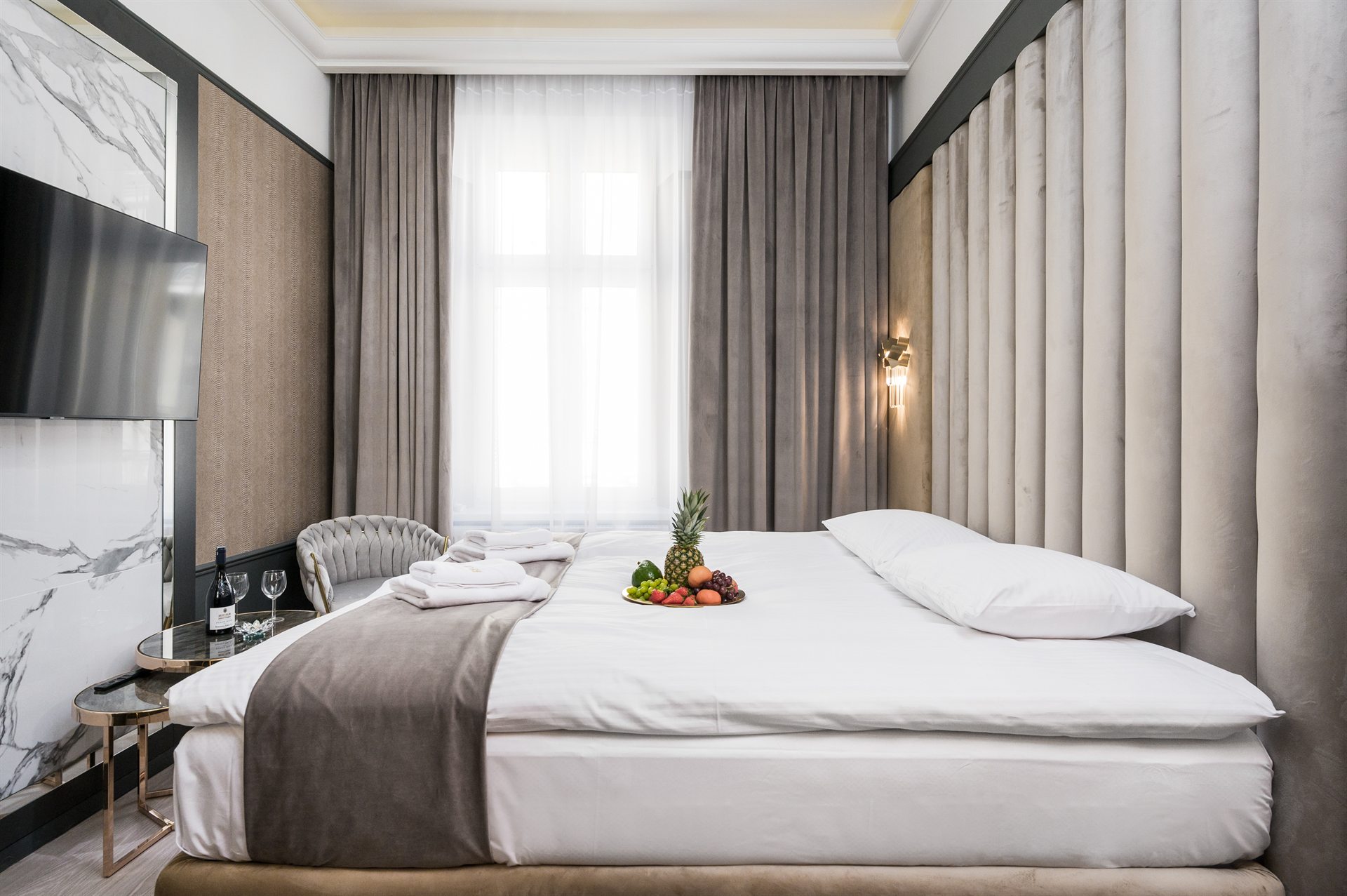 Elegancka sypialnia z łóżkiem, owocami i butelką wina na stoliku