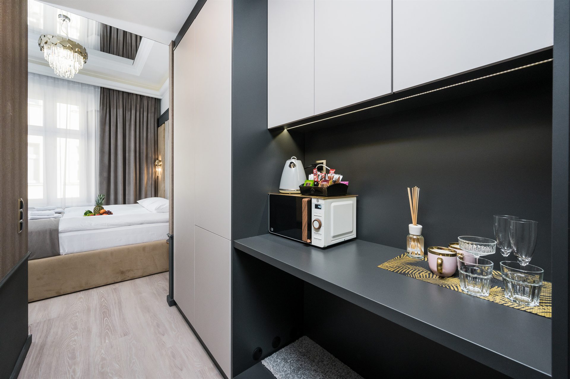 Kącik kuchenny z mikrofalówką, czajnikiem i owocami na stole w tle