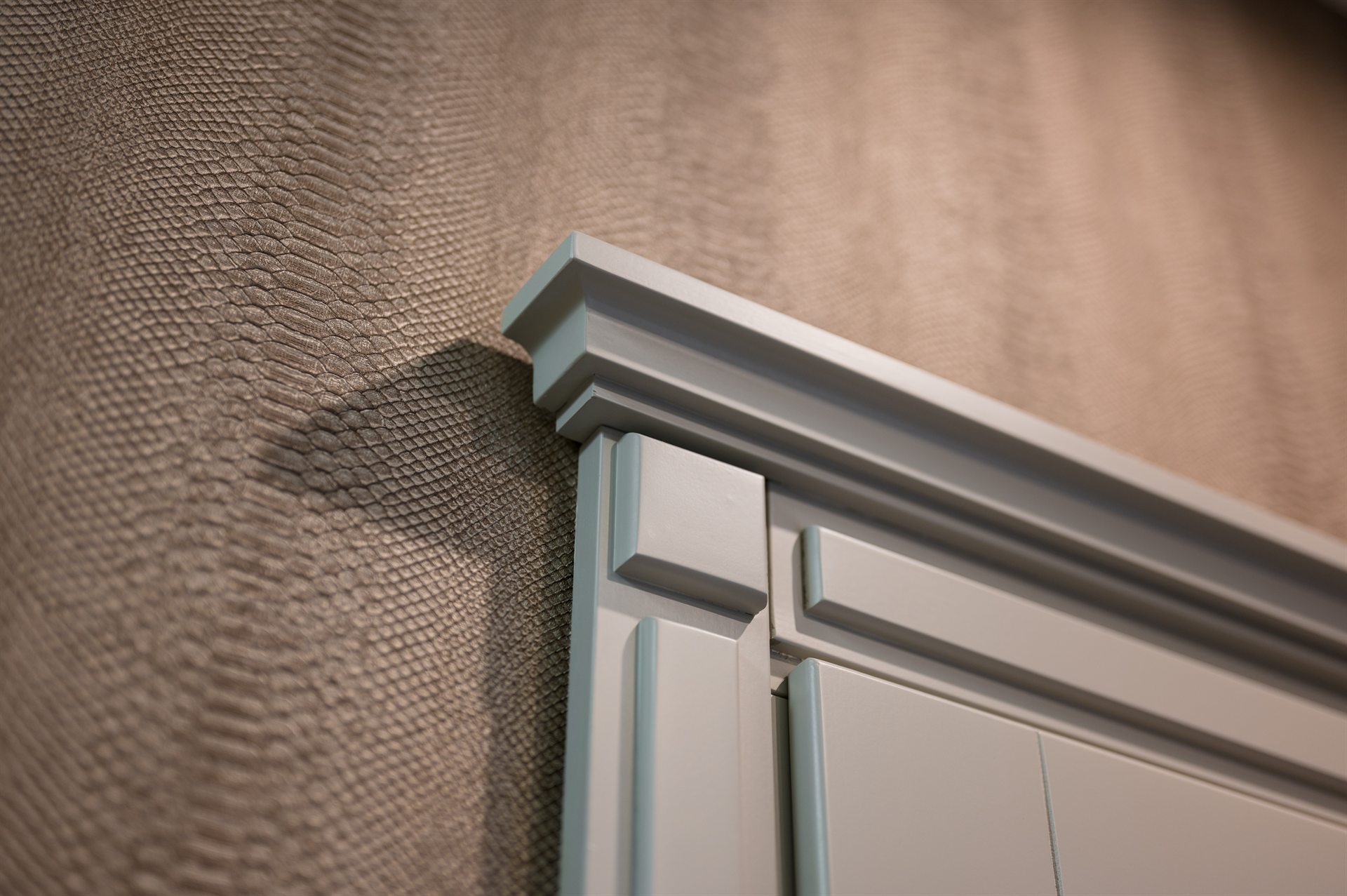 Górna krawędź mebla w jasnym kolorze na tle fakturowanej tapety