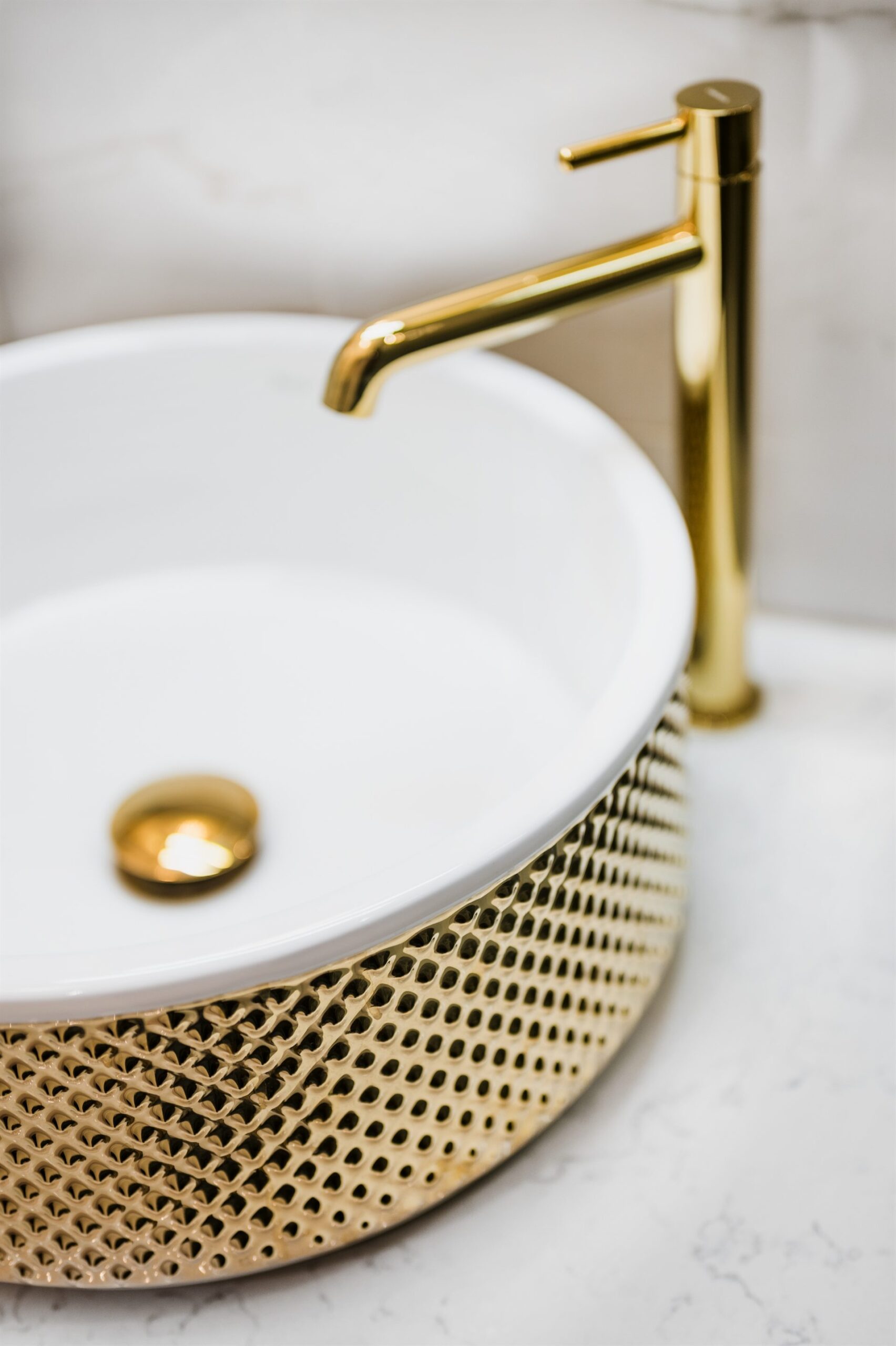 Biały zlew z złotą armaturą i ozdobnym, siatkowym wykończeniem