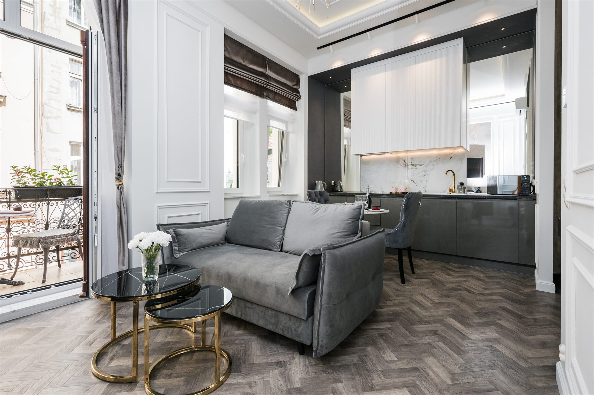 Nowoczesny salon z szarym sofą, złotymi stolikami i kuchnią w tle