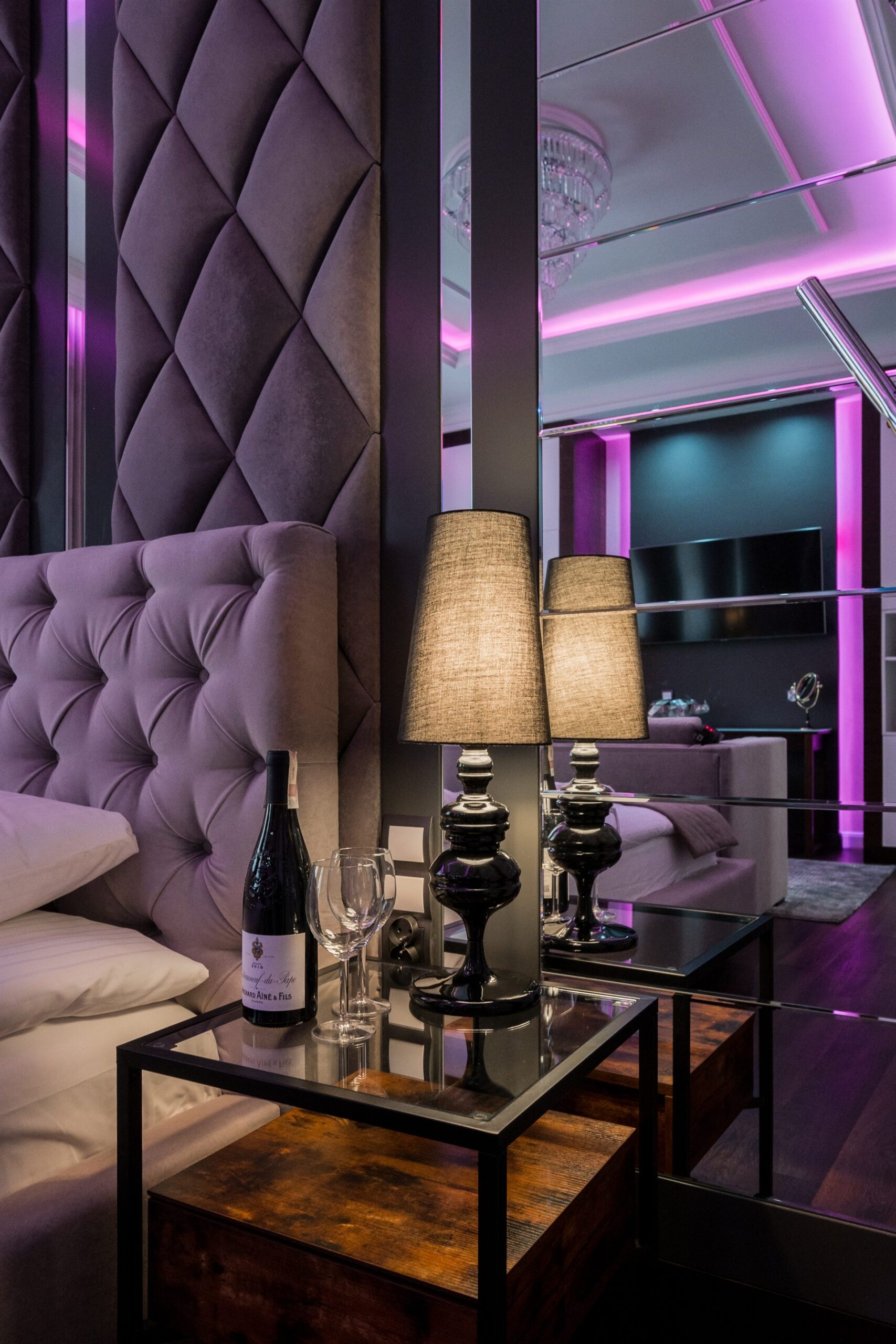 Elegancka sypialnia z fioletowym zagłówkiem i lampkami na stoliku nocnym