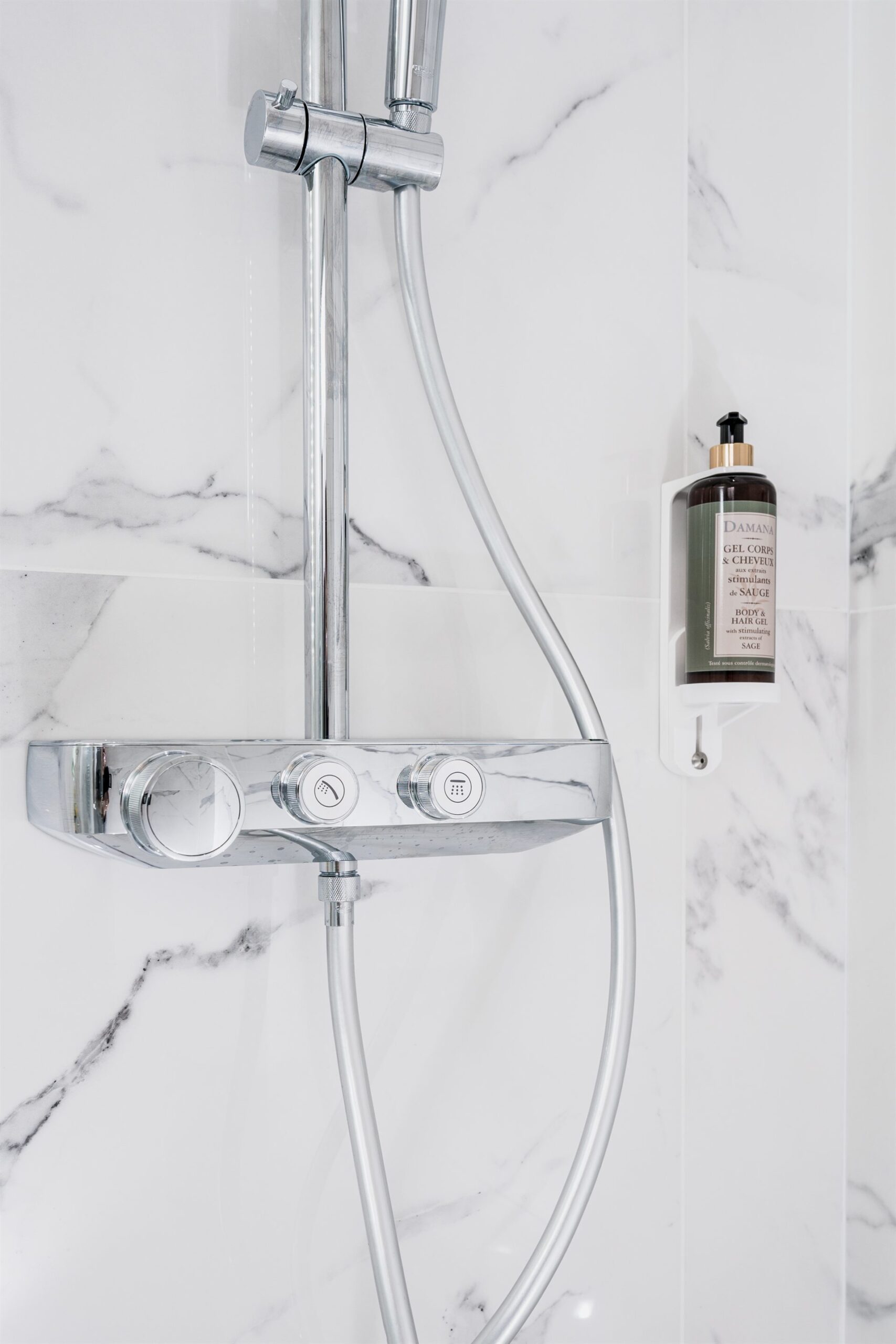 Wysoka, chromowana bateria prysznicowa na tle marmurowych płytek