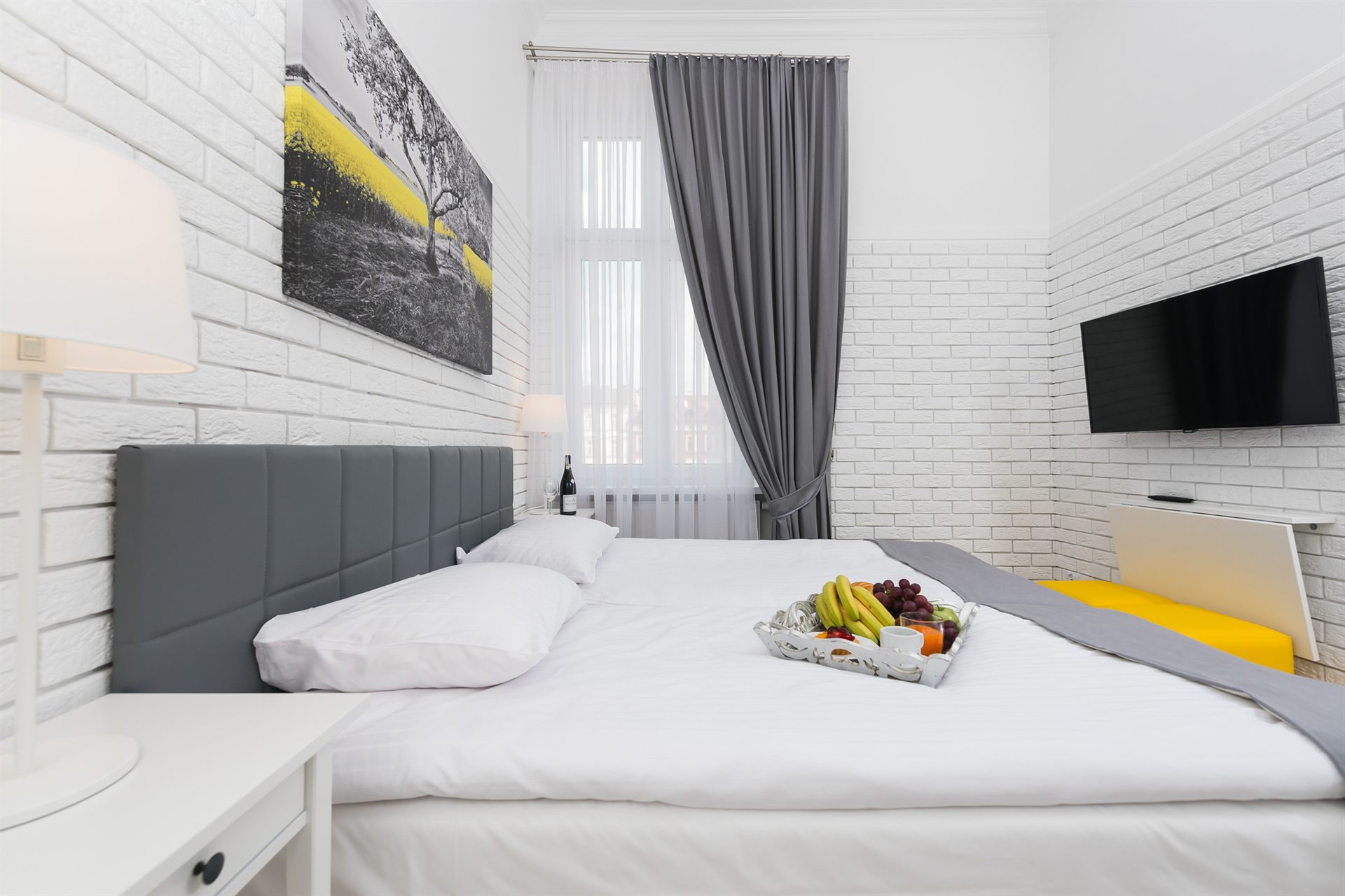 Nowoczesna sypialnia z dużym łóżkiem, szarymi zasłonami i owocami na stoliku
