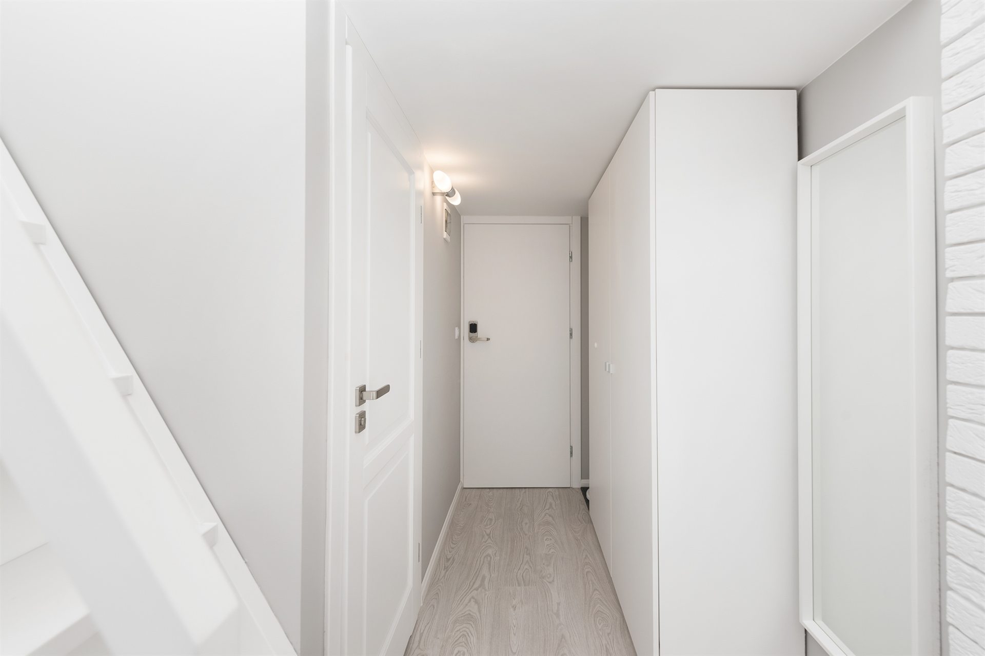 Jasny korytarz z białymi ścianami, schodami i drzwiami w tle