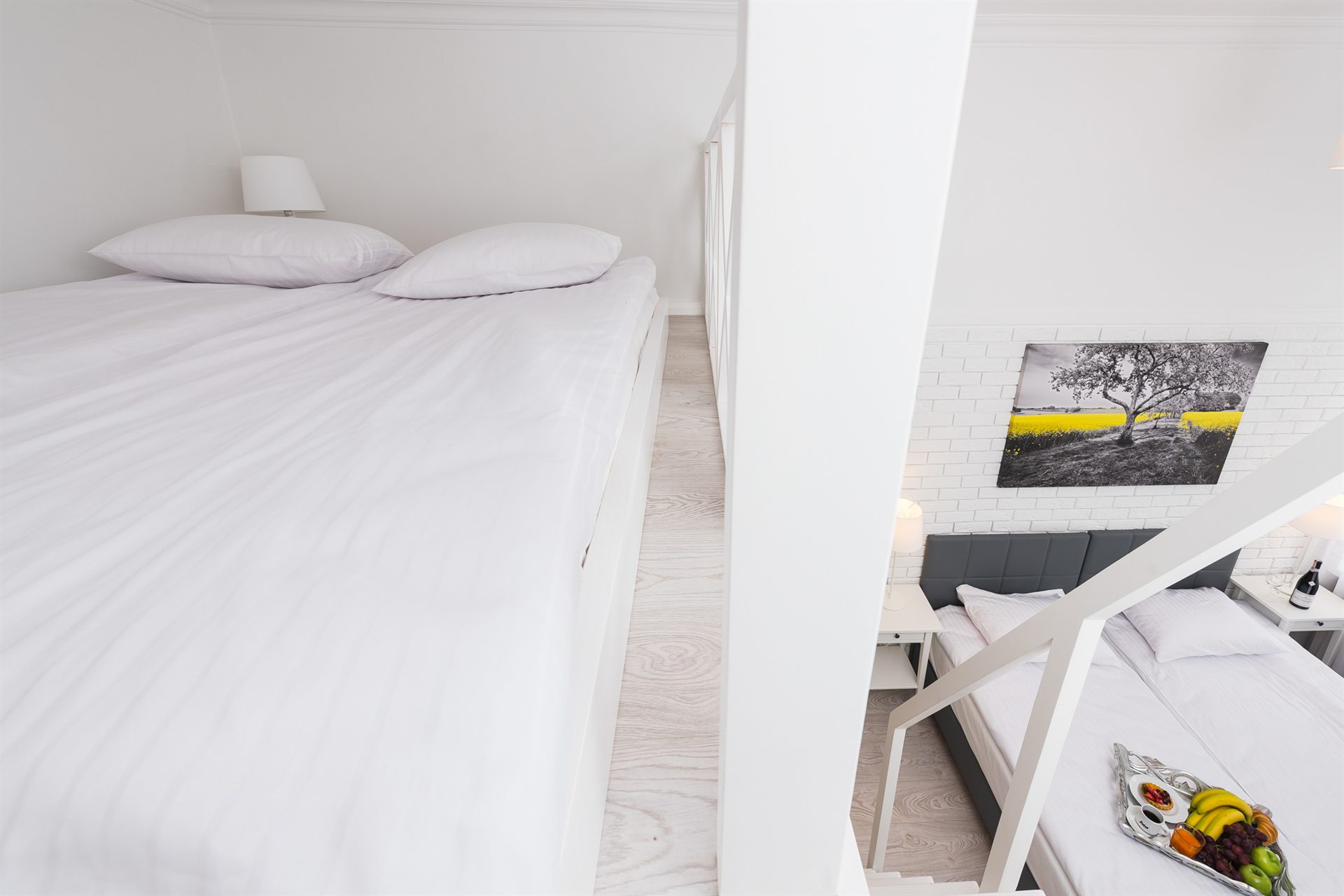 Dwa łóżka w jasnym wnętrzu, na ścianie obraz z drzewem i żółtym polem