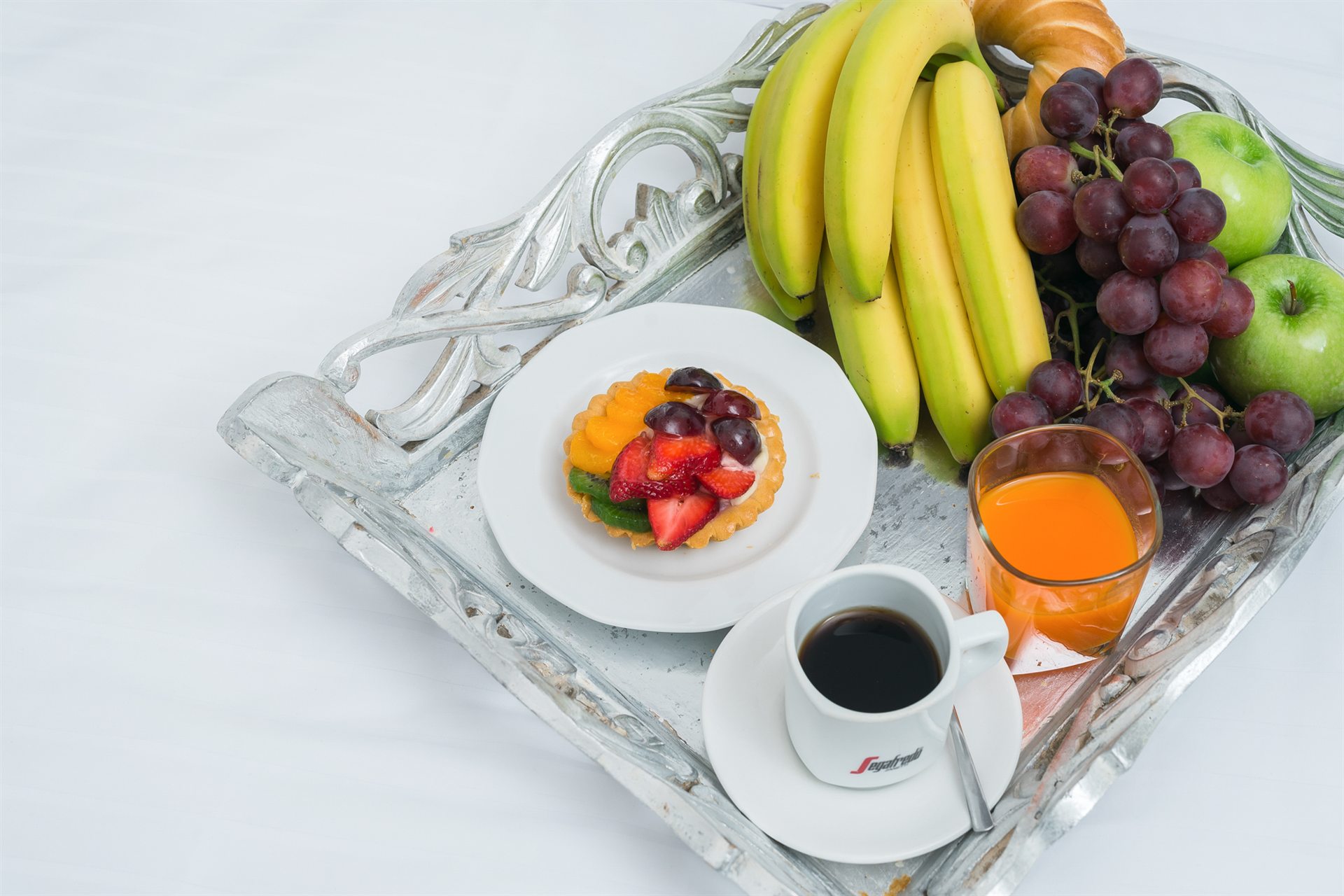 Taca z owocami, ciastkiem i filiżanką kawy na białym tle