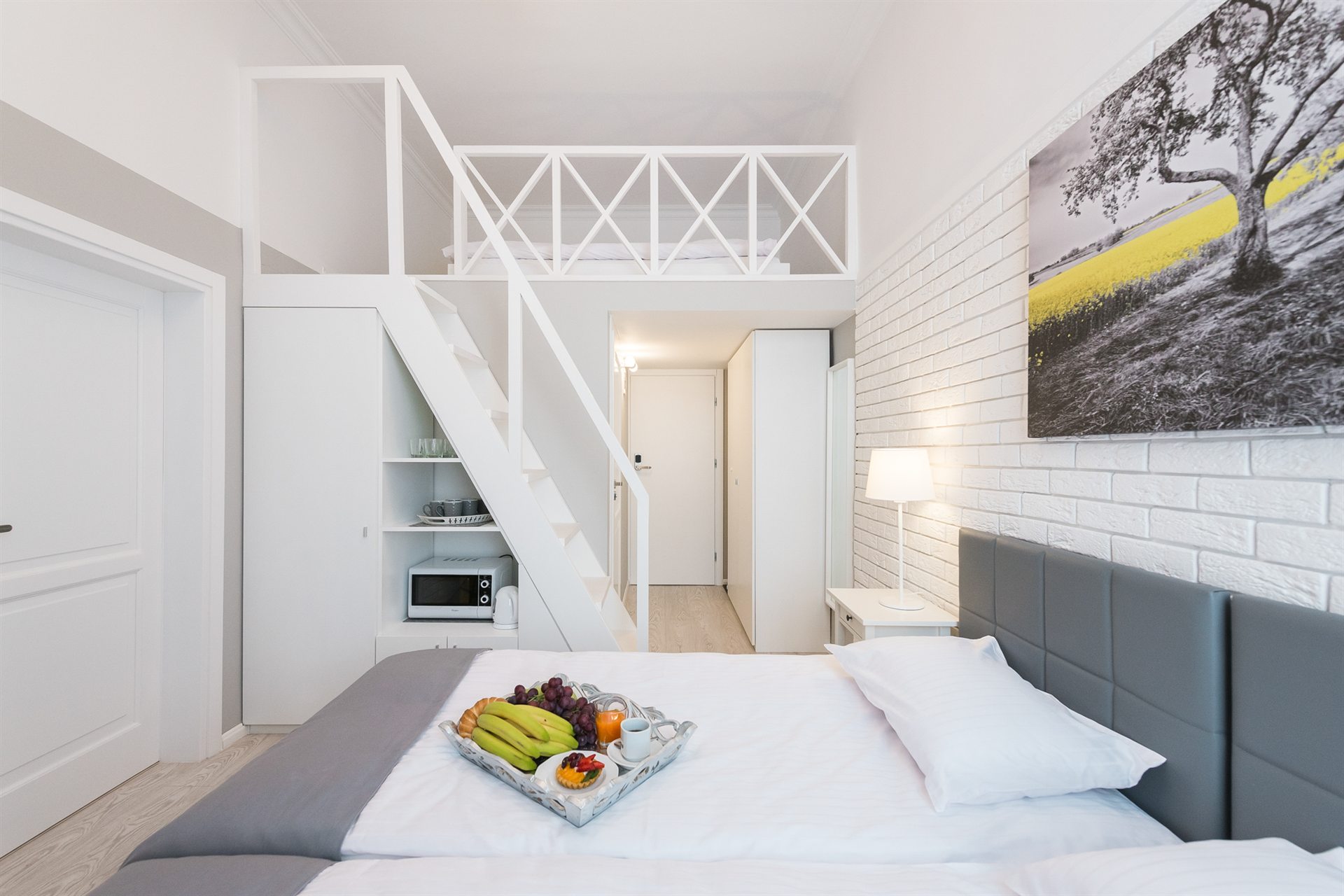 Przytulna sypialnia z antresolą, łóżko z owocami na tacy i lampą nocną
