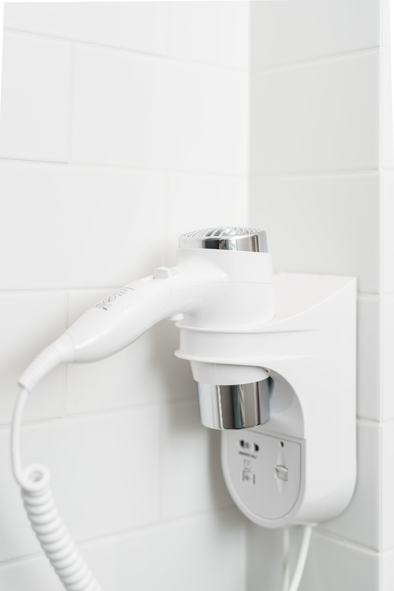 Suszarka do włosów zamontowana na ścianie w łazience, biała z chromowanymi elementami