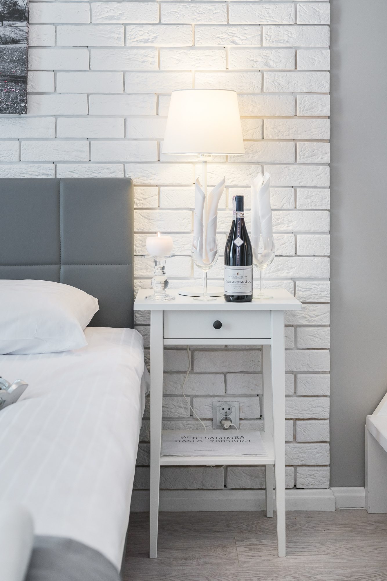 Biała lampka, wino i świeca na nocnym stoliku obok łóżka