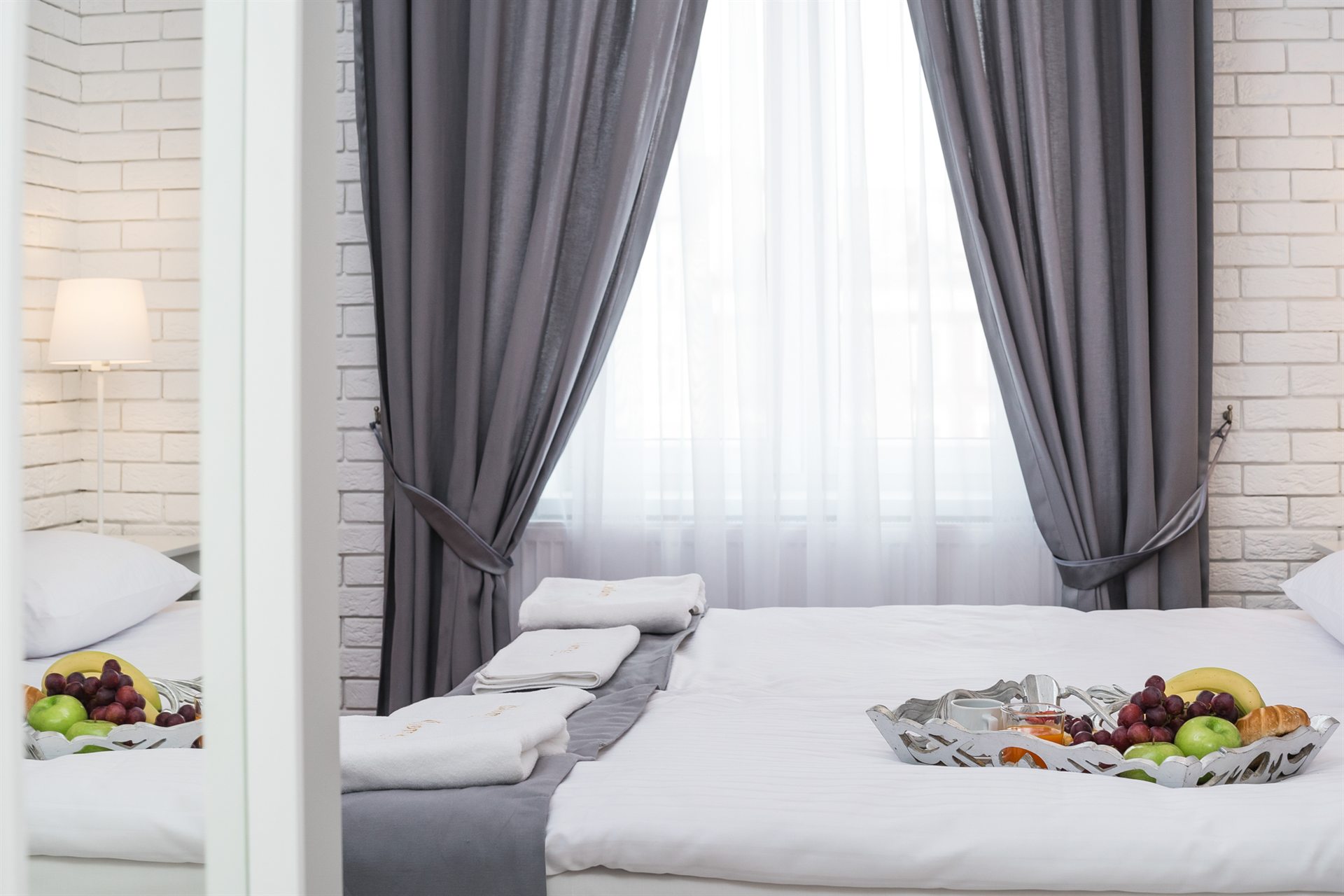 Jasna sypialnia z dużym oknem, na łóżku kosz owoców i ręczniki